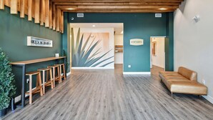 A reception area with a wooden reception desk, bar stools, a sofa, and a wall with a plant and abstract art. - Espadin Condos II (Denver)