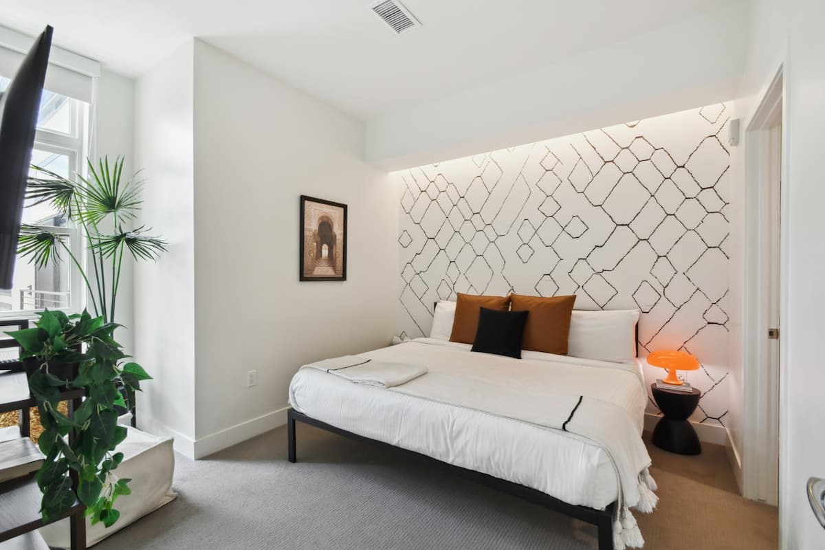 Une chambre à coucher moderne avec une tête de lit à motifs géométriques, un lit bien fait, une table de chevet avec une lampe et un tableau encadré au mur.