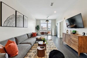 A modern living room with a sectional sofa, a coffee table, a TV, and artwork on the wall. - Espadin Condos II (Denver)