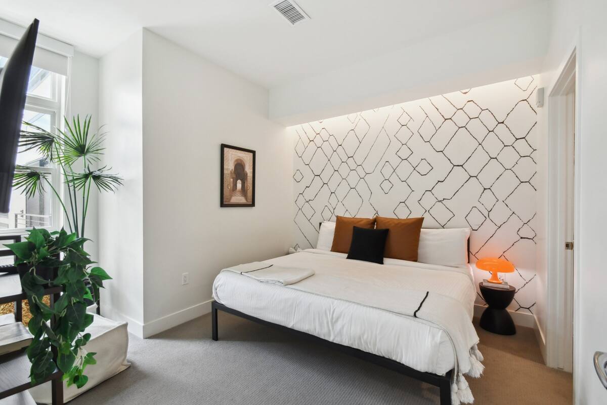 Une chambre à coucher moderne avec une tête de lit à motifs géométriques, un lit bien fait, une table de chevet avec une lampe et un tableau encadré au mur.