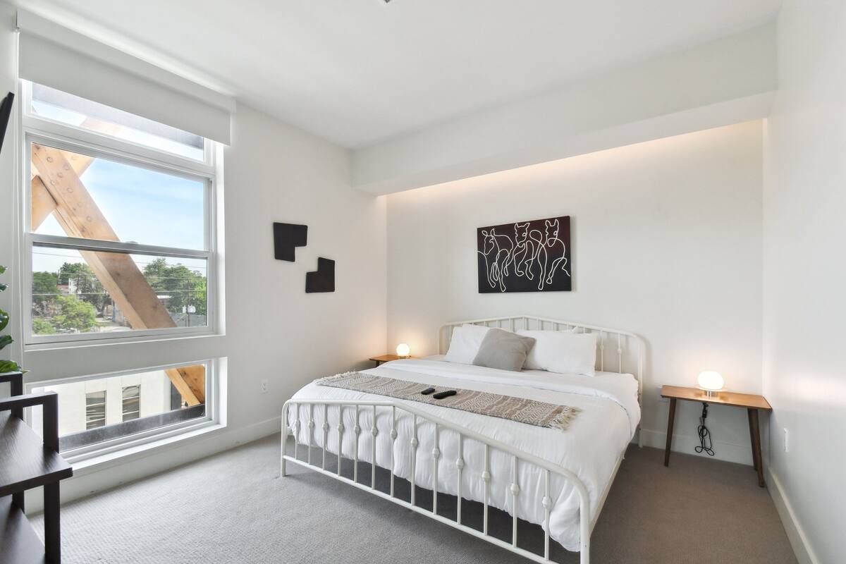 Une chambre avec un lit en métal blanc, une grande fenêtre et une vue sur l’extérieur.