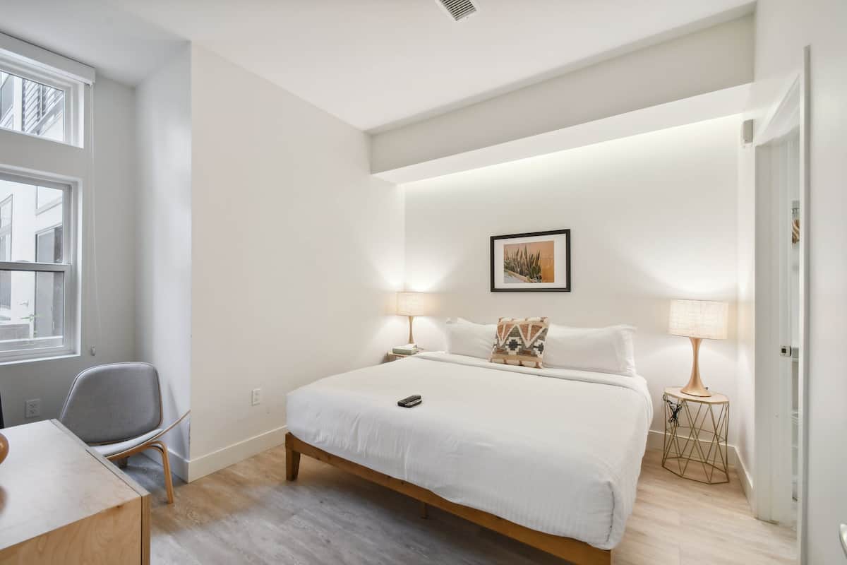 Ein modernes Schlafzimmer mit einem großen Bett, zwei Nachttischlampen, einem Sessel und einem kleinen Tisch.