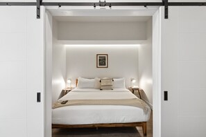 Ein schlicht eingerichtetes Schlafzimmer, mit einem zentrierten Bett und Nachttischen mit Lampen davor.