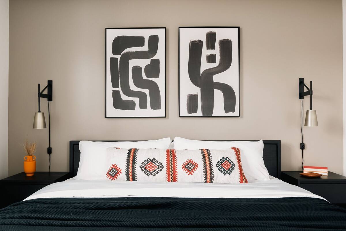 Une chambre d’hôtel avec un lit, deux lampes fixées au mur et deux tableaux abstraits.