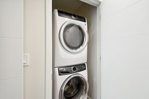 Eine übereinander gestellte Waschmaschine und ein Trockner in einem Badezimmer mit weißen Wänden und einem sichtbaren Lichtschalter.