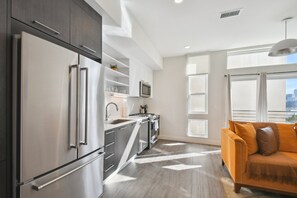 A modern kitchen with stainless steel appliances, a microwave, and a built-in oven. There is a window with a view of the city, and a sofa with cushions in the living area. - Espadin Condos I (Denver)