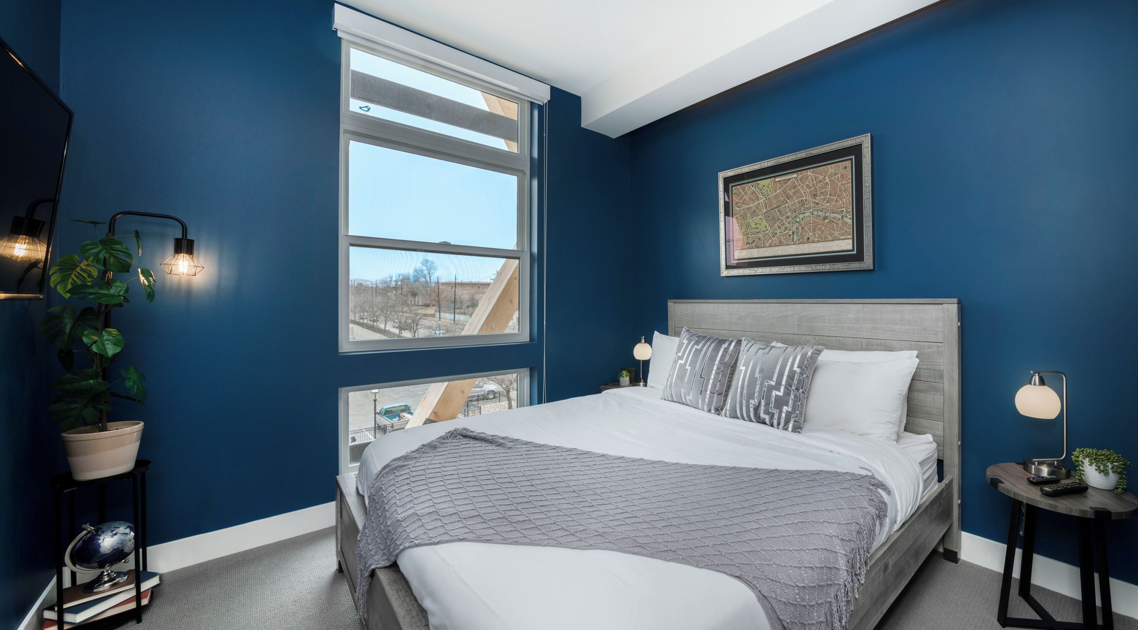 A bedroom with a large bed, two bedside tables, a window, and a cityscape view.