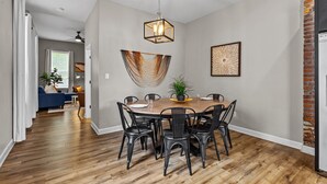 A dining area with a wooden table and black chairs, a hanging light fixture, and a brick wall. - Mysteries on Lemp | JZ Vacation Rentals (St. Louis)