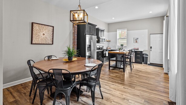 A modern kitchen with black cabinets, a wooden dining table, and a hanging light fixture. - Mysteries on Lemp | JZ Vacation Rentals (St. Louis)