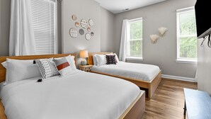 A hotel room with two beds, a wooden headboard, a wall-mounted lamp, and a flat-screen TV. - Mysteries on Lemp | JZ Vacation Rentals (St. Louis)