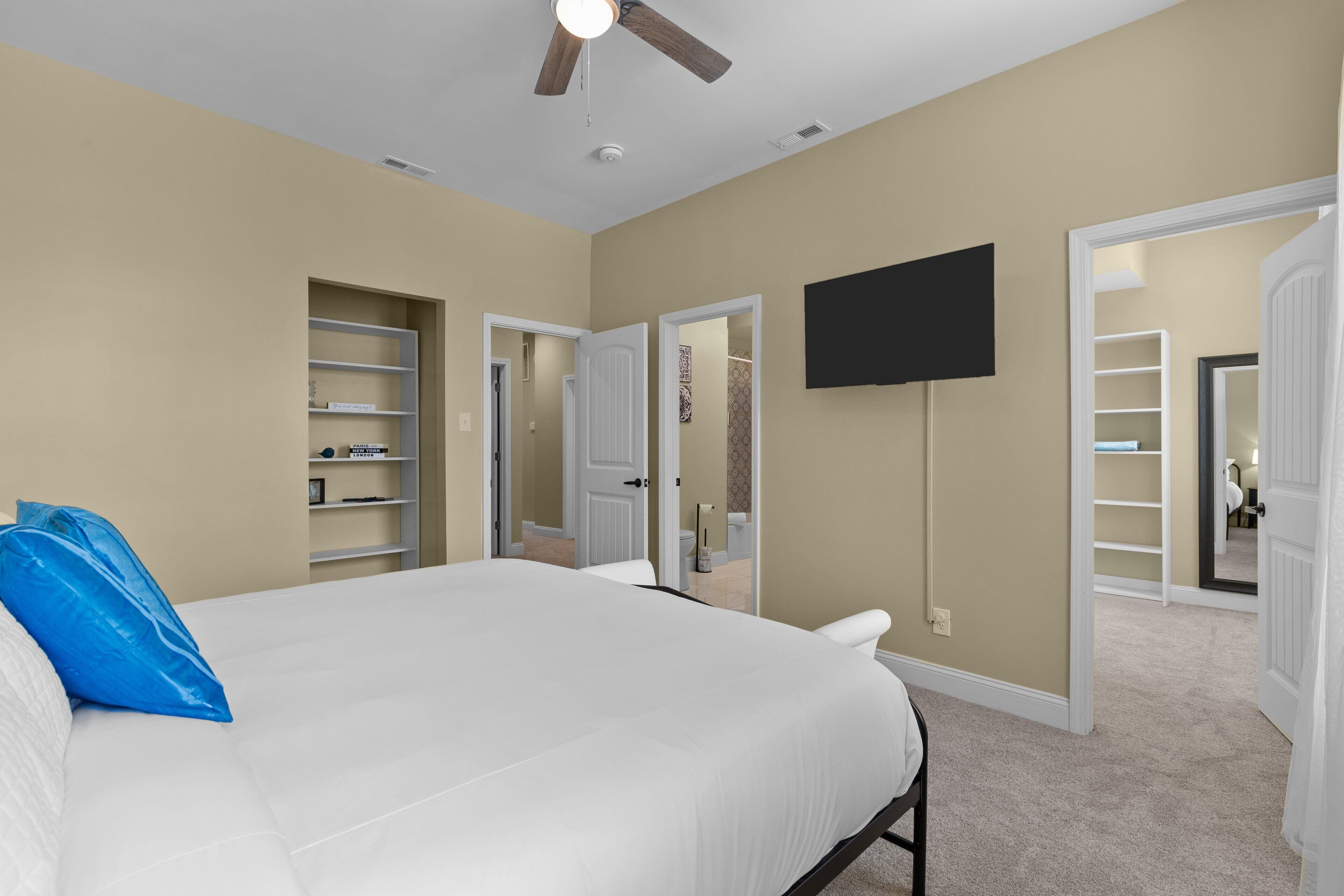 Une chambre à coucher comprenant un lit, un ventilateur de plafond, un téléviseur fixé au mur et un dressing.