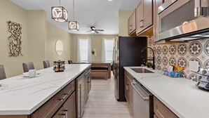 A modern kitchen with a large island, stainless steel appliances, and a ceiling fan. - Red Brick Hideaway | JZ Vacation Rentals (St. Louis)