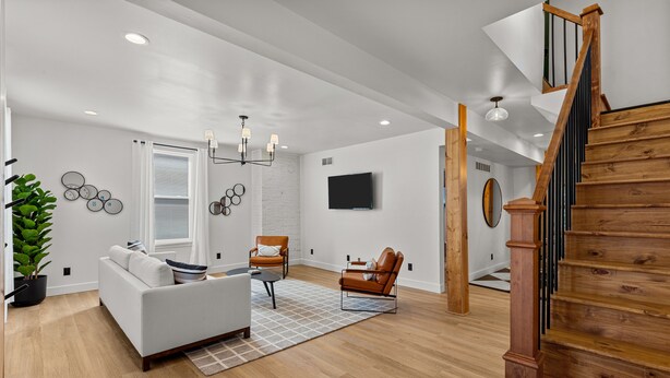 A modern living room with a white sofa, a brown leather chair, a wooden staircase, and a flat-screen TV mounted on the wall. - Wine Country Getaway | JZ Vacation Rentals (Washington)