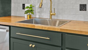 A kitchen with green cabinets, a stainless steel sink, and wooden shelves holding glassware. - Wine Country Getaway | JZ Vacation Rentals (Washington)