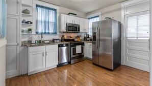 A kitchen with white cabinets, stainless steel appliances, a granite countertop, and wooden flooring. - Forest Park Oasis | JZ Vacation Rentals (St. Louis)