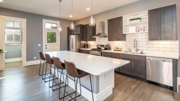 A modern kitchen with a large island, dark cabinets, stainless steel appliances, and pendant lighting. - Parkside Comfort | JZ Vacation Rentals (St. Louis)