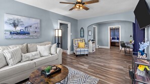 A living room with a sofa, coffee table, and a ceiling fan. There is a painting on the wall and a dining area in the background. - Sweet Cherry Escape | JZ Vacation Rentals (Warrenton)