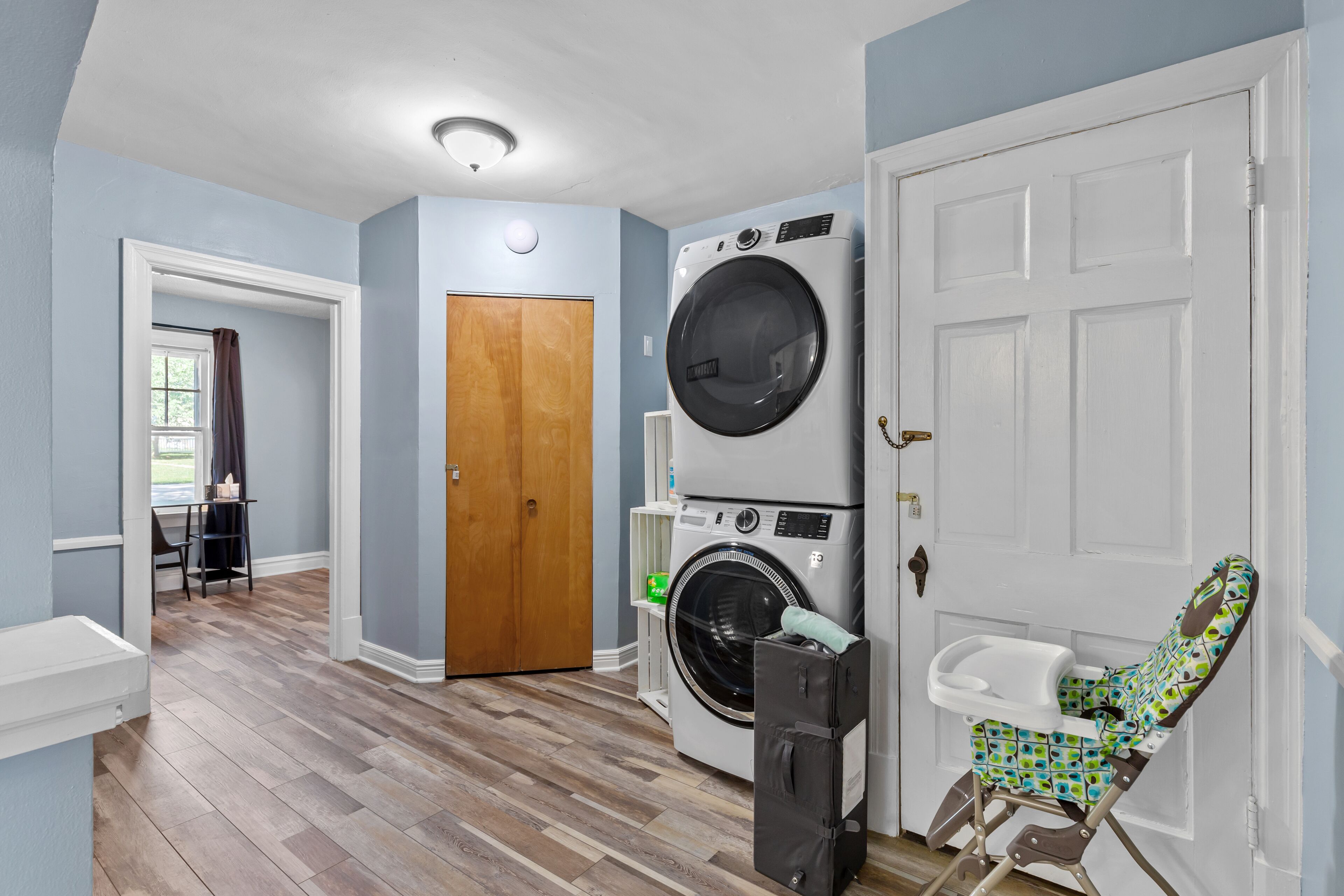 A laundry room with a stacked washer and dryer, a wooden door, and a baby changing station.