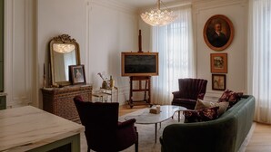 Ein klassischer Wohnraum mit einem Marmortisch, einem grünen Sofa, einem roten Sessel und einem großen Gemälde an der Wand.