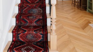 Eine Treppe mit einem roten Teppichmuster, Holzhandläufen und einem hellen Holzboden.
