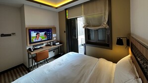 Una camera d'albergo con un letto, una scrivania con televisore e una finestra con tende.