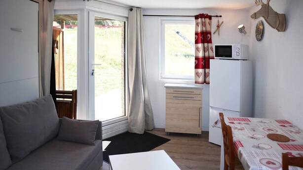 A compact living space with a sofa, a small table, a kitchenette with a fridge, and a dining area with a table and chairs. - Lovely 4-person studio with ski in ski out (LES ORRES 1650)