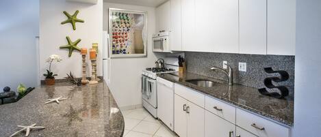 A modern kitchen with white cabinets, granite countertops, and a microwave.