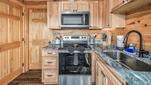 Una cocina compacta con muebles de madera, horno de acero inoxidable, microondas y un lavamanos con grifo.