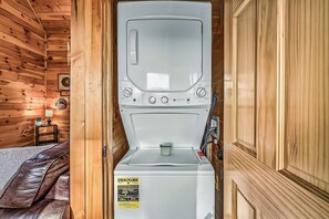 Vue de face d’un lave-linge à chargement frontal blanc, situé dans une pièce d’une cabane en bois.