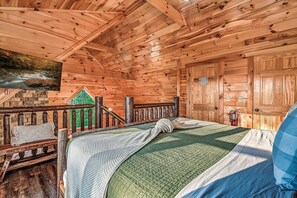 L’intérieur d’un chalet en bois, avec un lit, un tableau, une cheminée et une vue sur une forêt.