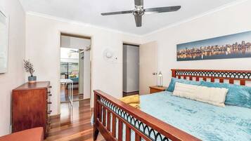 A bedroom with a bed, a ceiling fan, a wooden headboard, a nightstand, a lamp, and a painting of a cityscape.