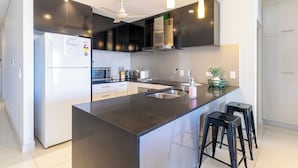A modern kitchen with a central island, black cabinets, stainless steel appliances, and a ceiling fan.