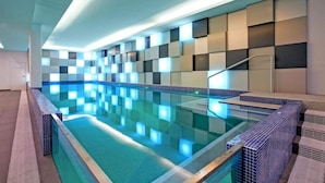 A modern indoor swimming pool with a geometric wall design and a clear blue pool.