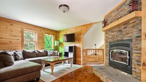 Un salon chaleureux avec une cheminée en pierre, des murs en bois, un canapé et un téléviseur.