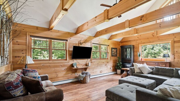 L’intérieur d’une cabane en rondins, avec une grande fenêtre, un téléviseur à écran plat et une cheminée.