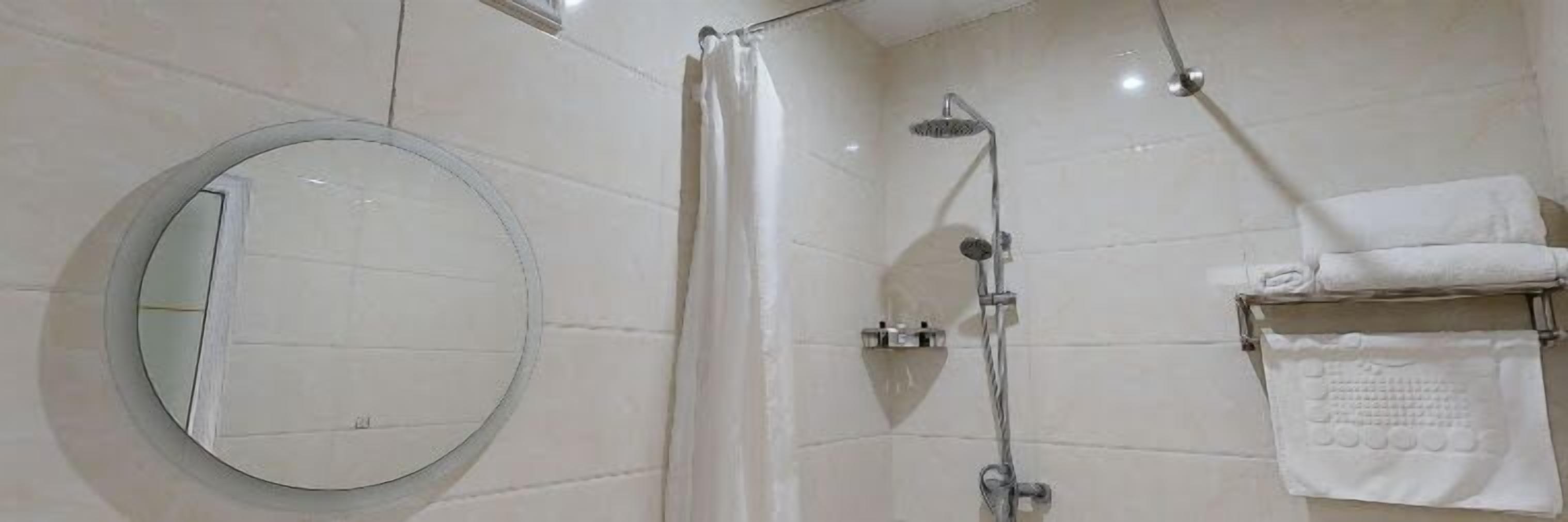 Ein Badezimmer mit rundem Spiegel, einer Dusche mit Duschbrause und einem Handtuchhalter mit gefalteten Handtüchern.