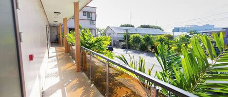A balcony with a glass railing overlooking a street with buildings and greenery.