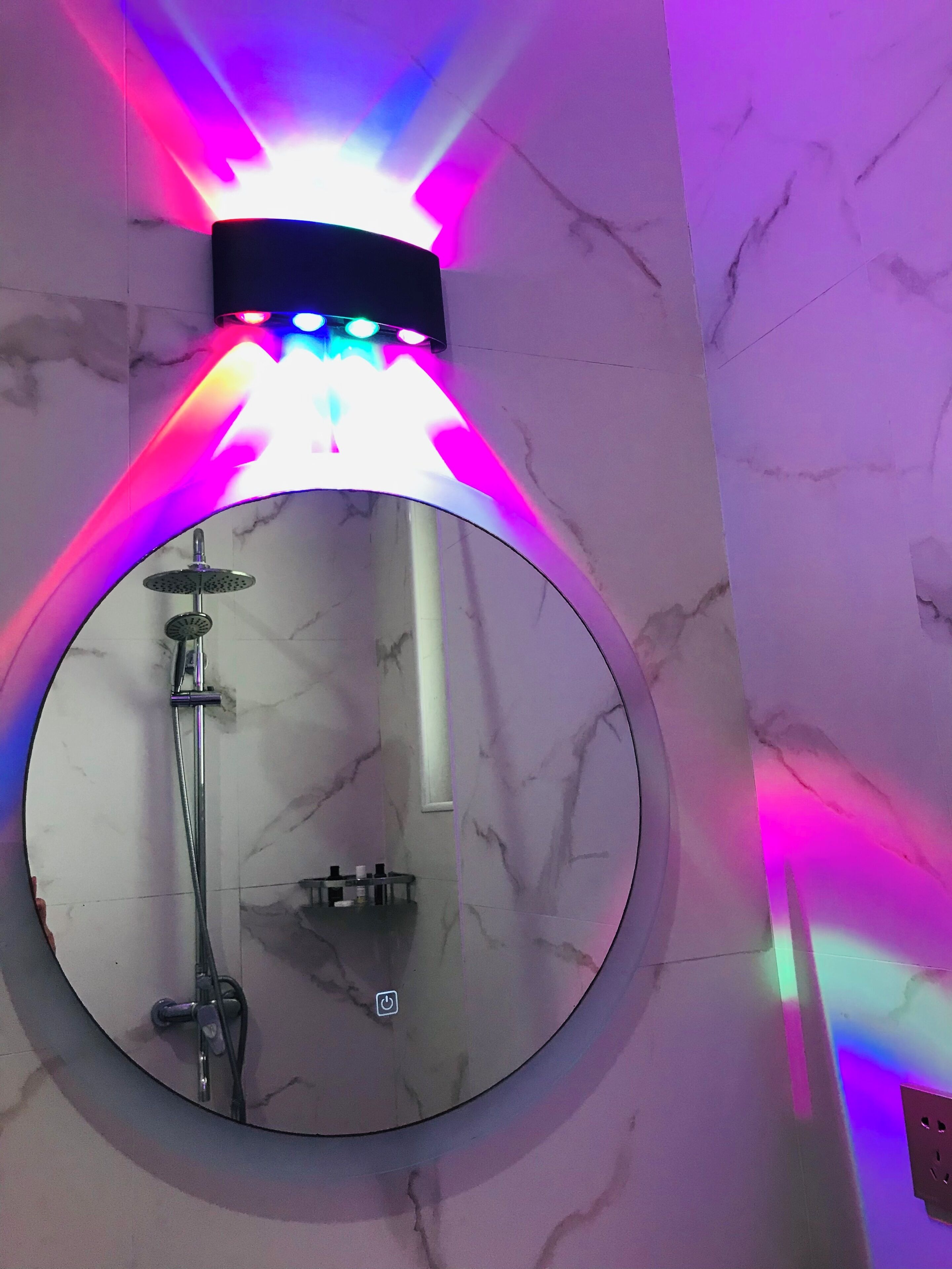 A circular mirror with a shower head below it, mounted on a wall with a marble pattern.