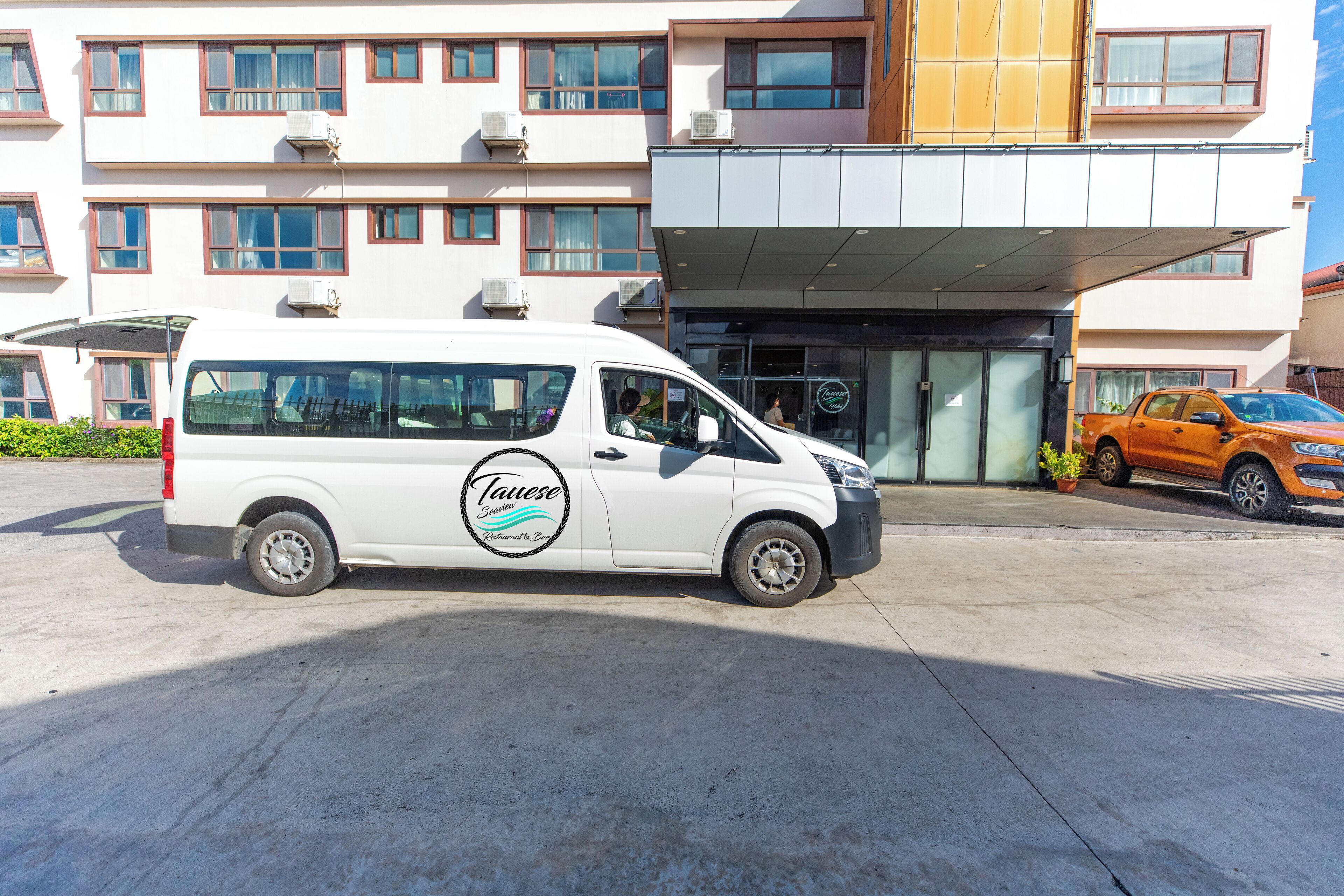 Un furgone bianco parcheggiato di fronte a un edificio con ingresso moderno e numerose finestre.