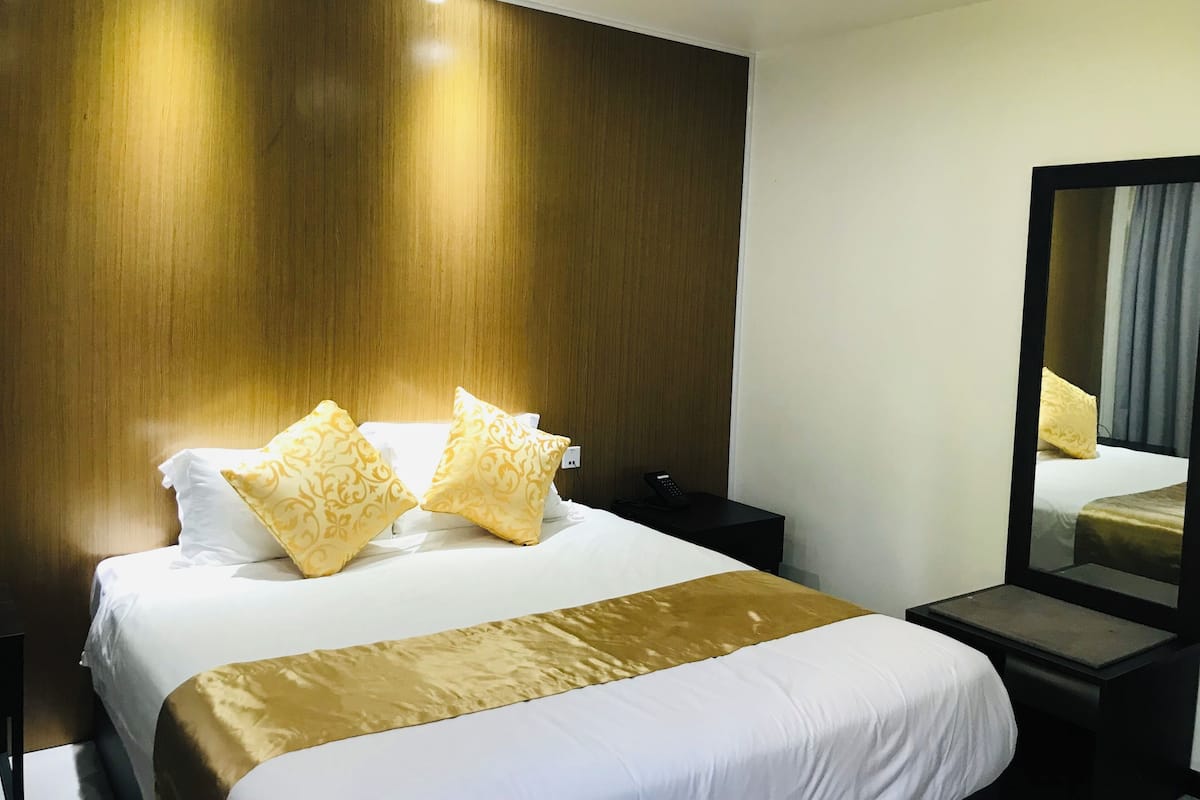 A hotel room with a large bed, two bedside tables, a nightstand, a mirror, and a wooden wall.