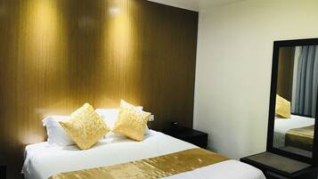 Habitación de hotel con una cama grande, dos mesitas de noche, un tocador, un espejo y una pared de madera.