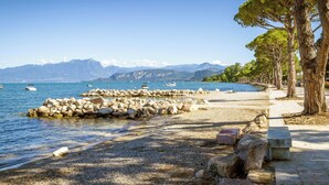 Un paysage côtier avec une plage de galets, une jetée en pierre et une rangée d’arbres.