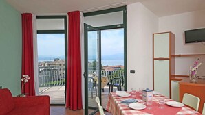 Une chambre avec un balcon, une table à manger dressée pour deux personnes et un téléviseur fixé au mur.