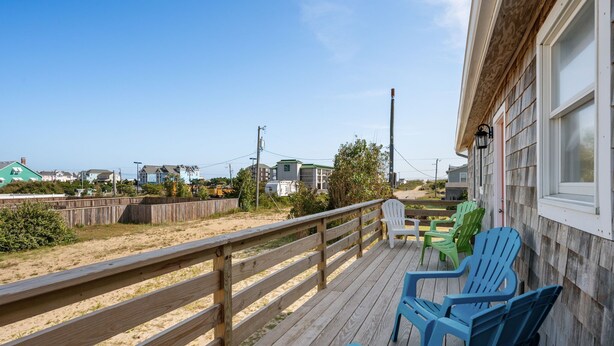 Eine Holzterrasse mit blauen Stühlen und einem Hollerleger, der auf einen Strand blickt.