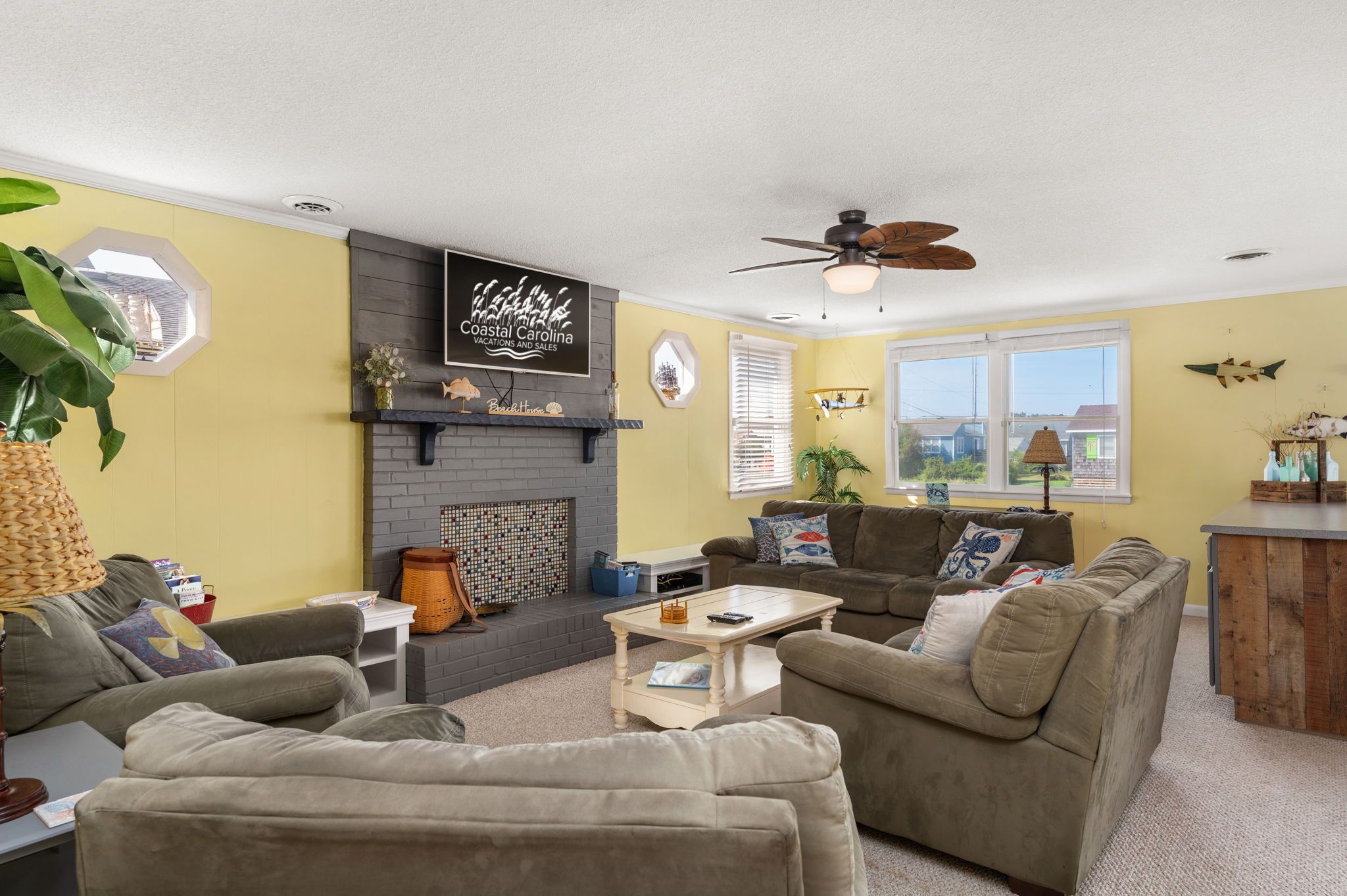 A living room with a fireplace, a ceiling fan, and a view of the outdoors.