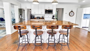 A modern kitchen with white cabinets, a wooden island with bar stools, stainless steel appliances, and pendant lighting. - "SALT WIND" HAS GULF VIEWS, STEPS TO BEACH, SECLUDED & PEACEFUL! (Mexico Beach)