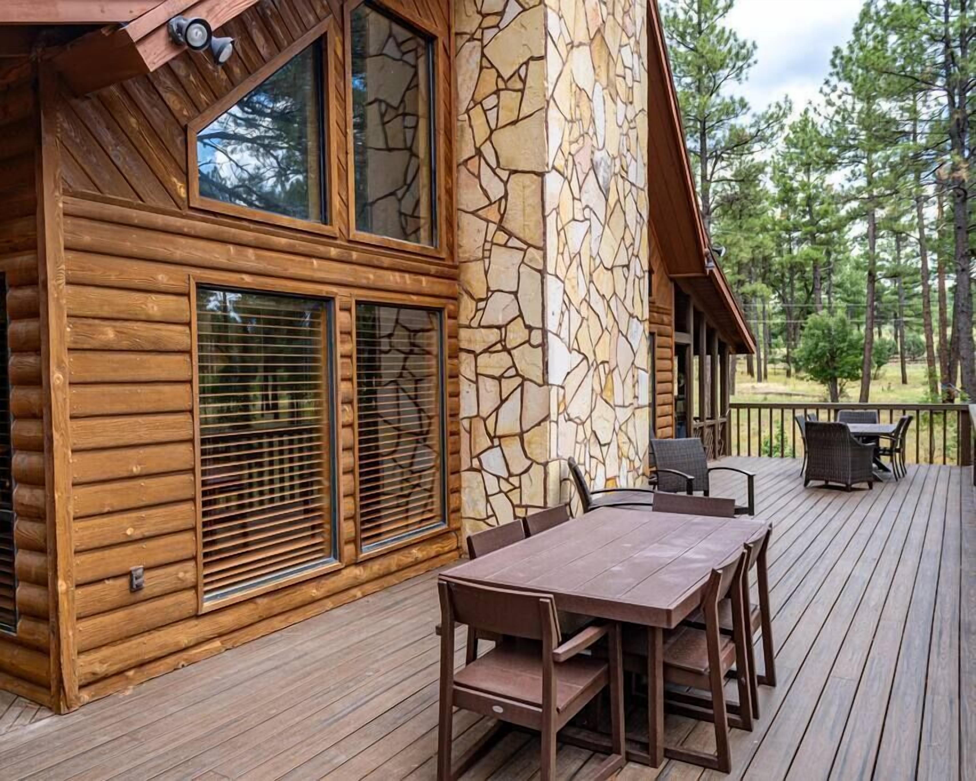 Una cabaña de madera con fachada de piedra, una terraza con mesa y sillas, y vistas a árboles.