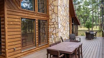Una cabaña de madera con fachada de piedra, una terraza con mesa y sillas, y vistas a árboles.