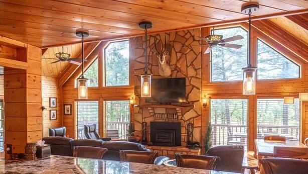 L’intérieur d’une cabane en rondins, avec une cheminée en pierre, de grandes fenêtres et un coin bar.