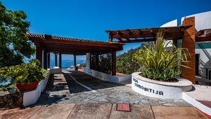 A covered outdoor area with a stone pathway leading to a building entrance, surrounded by potted plants and a clear view of the sea. - Suite 2 - Casa Samo Conchas Chinas (Puerto Vallarta)